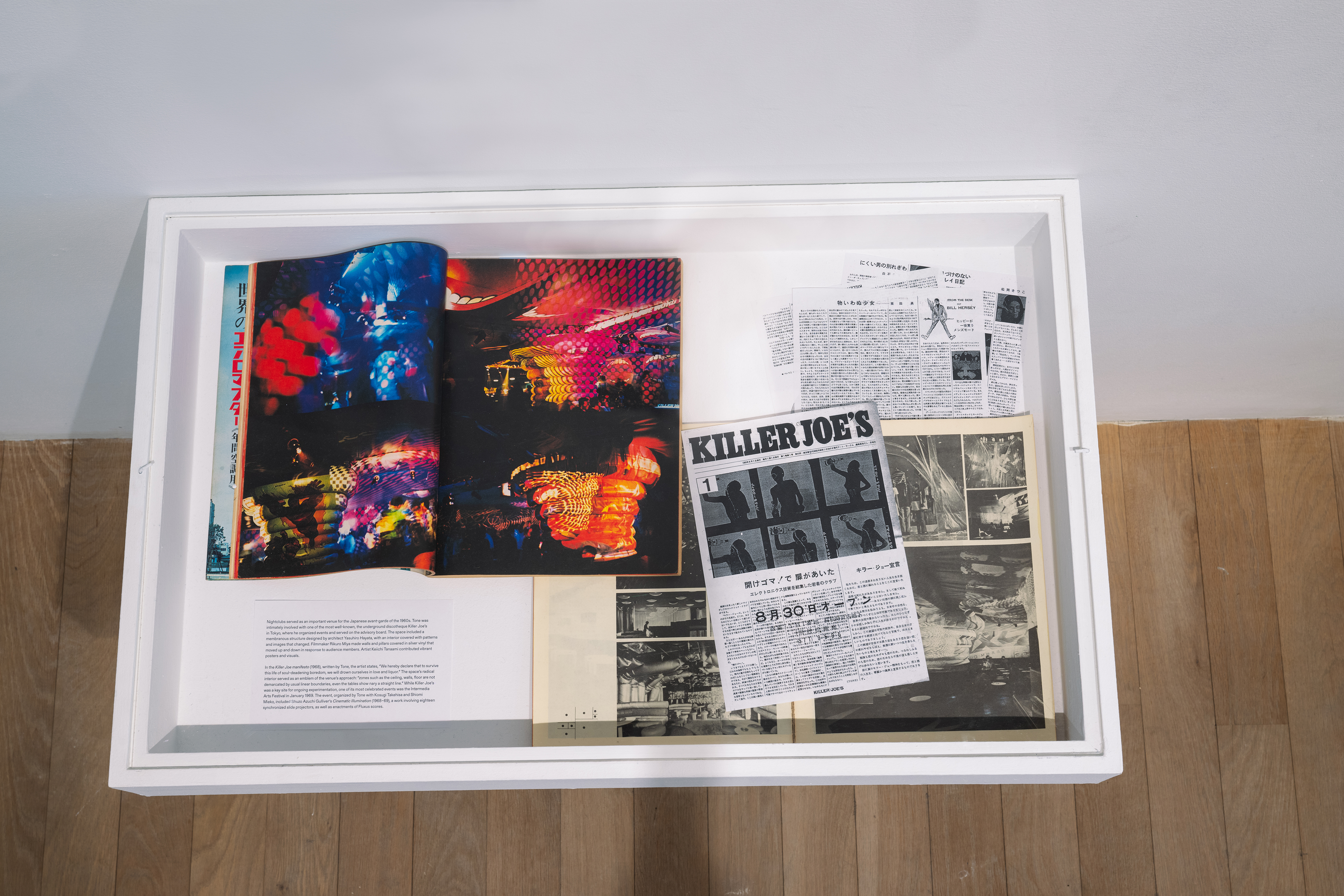 Color photograph of a vitrine from above. Various ephemera including magazines and fliers are placed inside.