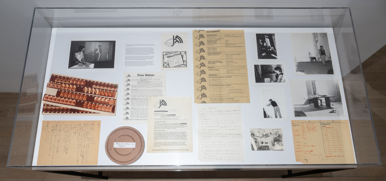 Color photograph of a vitrine from above. Various ephemera including press releases, photographs, and notes are placed inside.