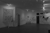 Numerous artworks appear on the walls of a white-walled gallery space.