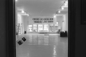 A view through a doorway into a white-walled gallery space with drawings on the walls and a banner on the windows.