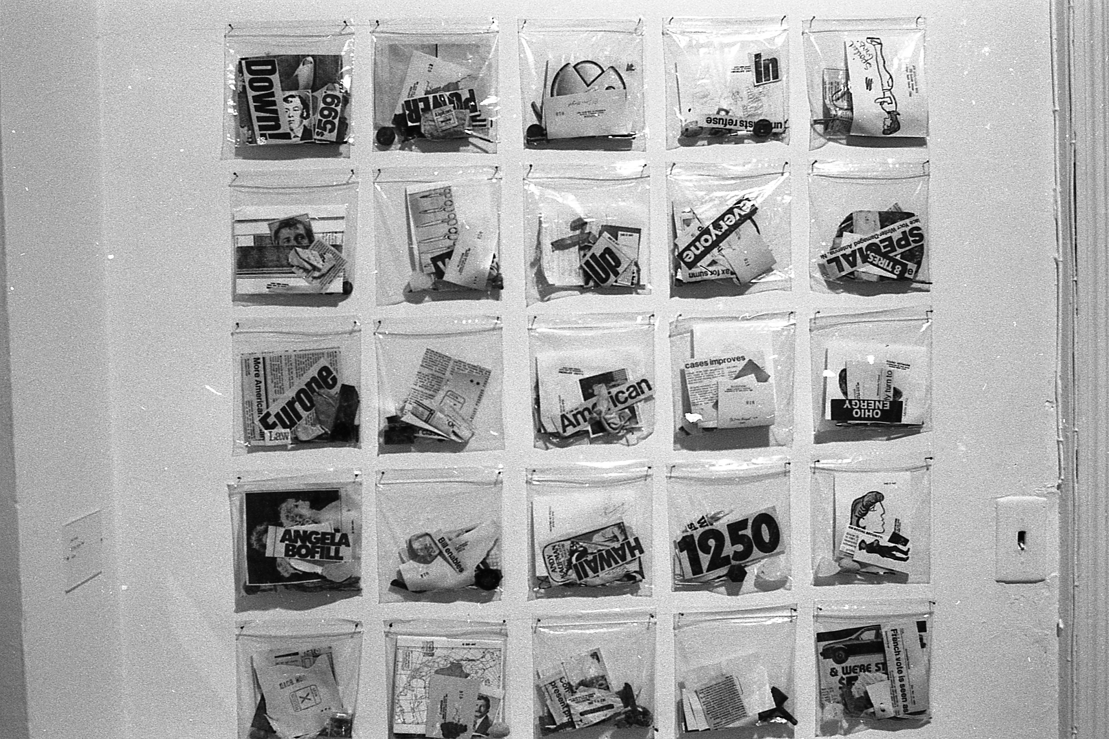 Numerous plastic bags of objects appear together on a white gallery wall.