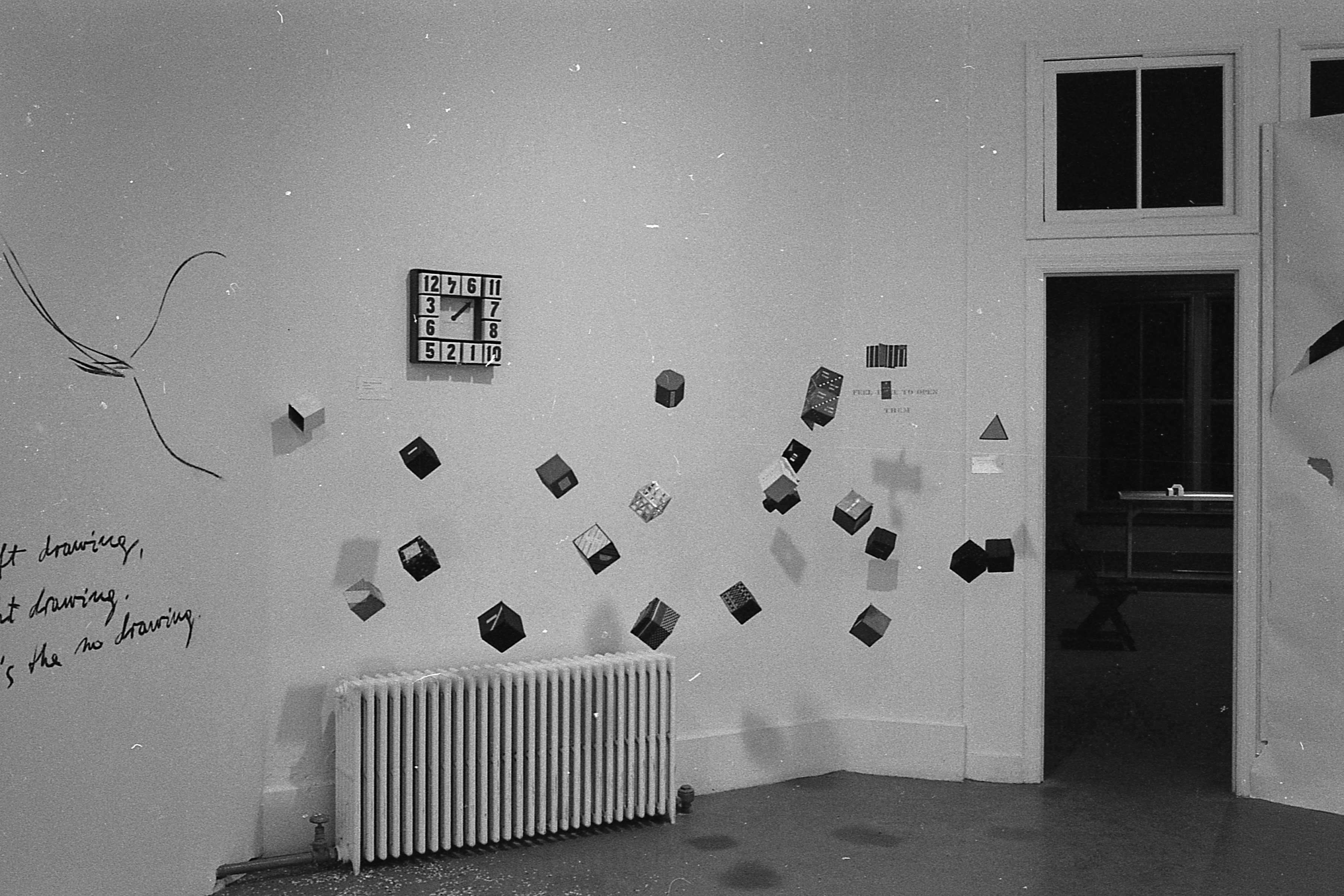 A number of sculpted objects lie suspended from the ceiling in front of a wall with other sculpted works and a nearby drawing is also visible.