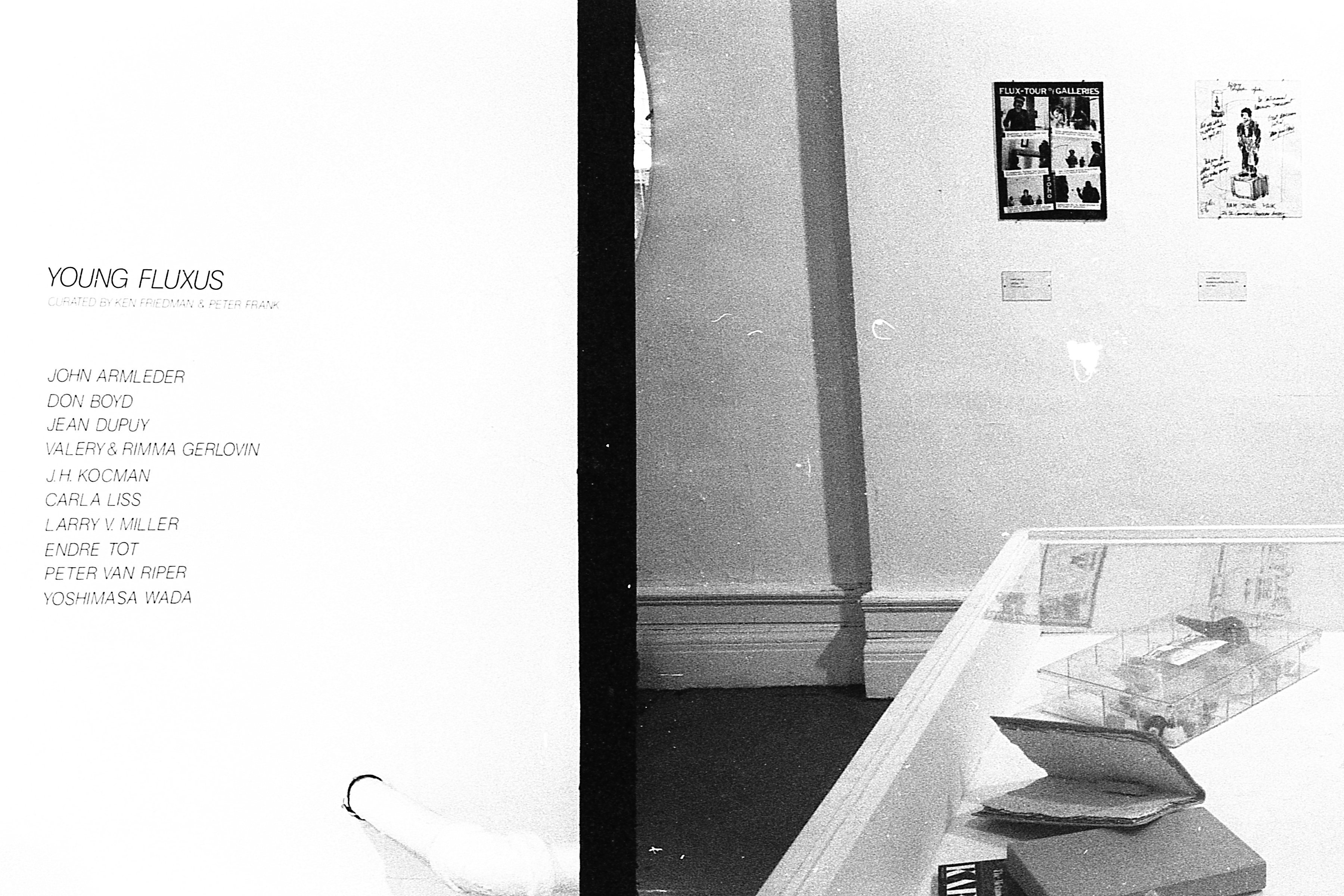 Exhibition wall text on the left next to a vitrine of objects and posters on the right back wall.