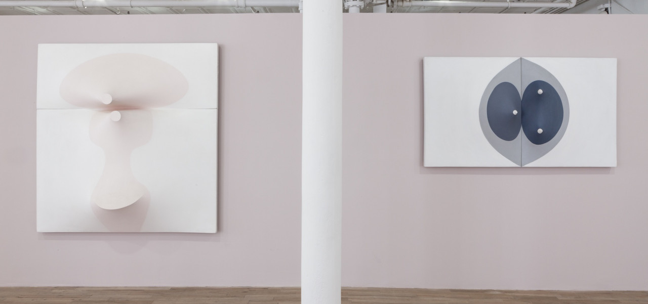 Two paneled works hang on either side of a white column on a light, mauve-colored wall. Both canvases are slightly three-dimensional, with elements that stretch in or out from their surfaces.