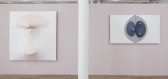 Two paneled works hang on either side of a white column on a light, mauve-colored wall. Both canvases are slightly three-dimensional, with elements that stretch in or out from their surfaces.