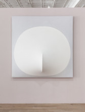 A square, gray canvas with a large white circle centered towards its bottom edge hangs on a light, mauve-colored wall. At the bottom center of the circle, the canvas stretches outward in a verticle line.