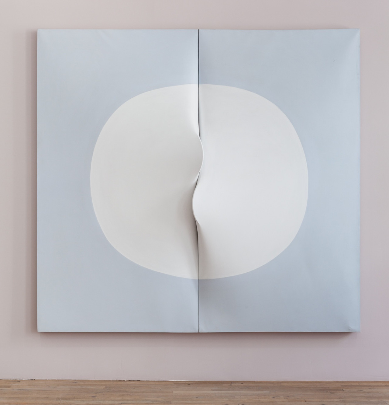 Two light blue panels of canvas displayed on a light mauve wall. The canvases are positioned side-by-side such that they form a square shape. Two semicircles are depicted on each of the canvases, which together form a white circle in the center of the two canvases. At the center of the circle, the edges of each of the canvases stretch outward to form two protruding flaps that curve towards and on top of the opposite canvases.