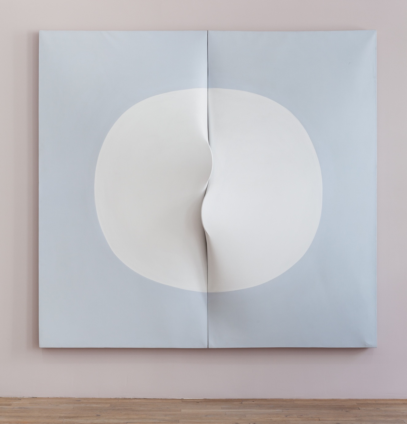 Two light blue panels of canvas displayed on a light mauve wall. The canvases are positioned side-by-side such that they form a square shape. Two semicircles are depicted on each of the canvases, which together form a white circle in the center of the two canvases. At the center of the circle, the edges of each of the canvases stretch outward to form two protruding flaps that curve towards and on top of the opposite canvases.