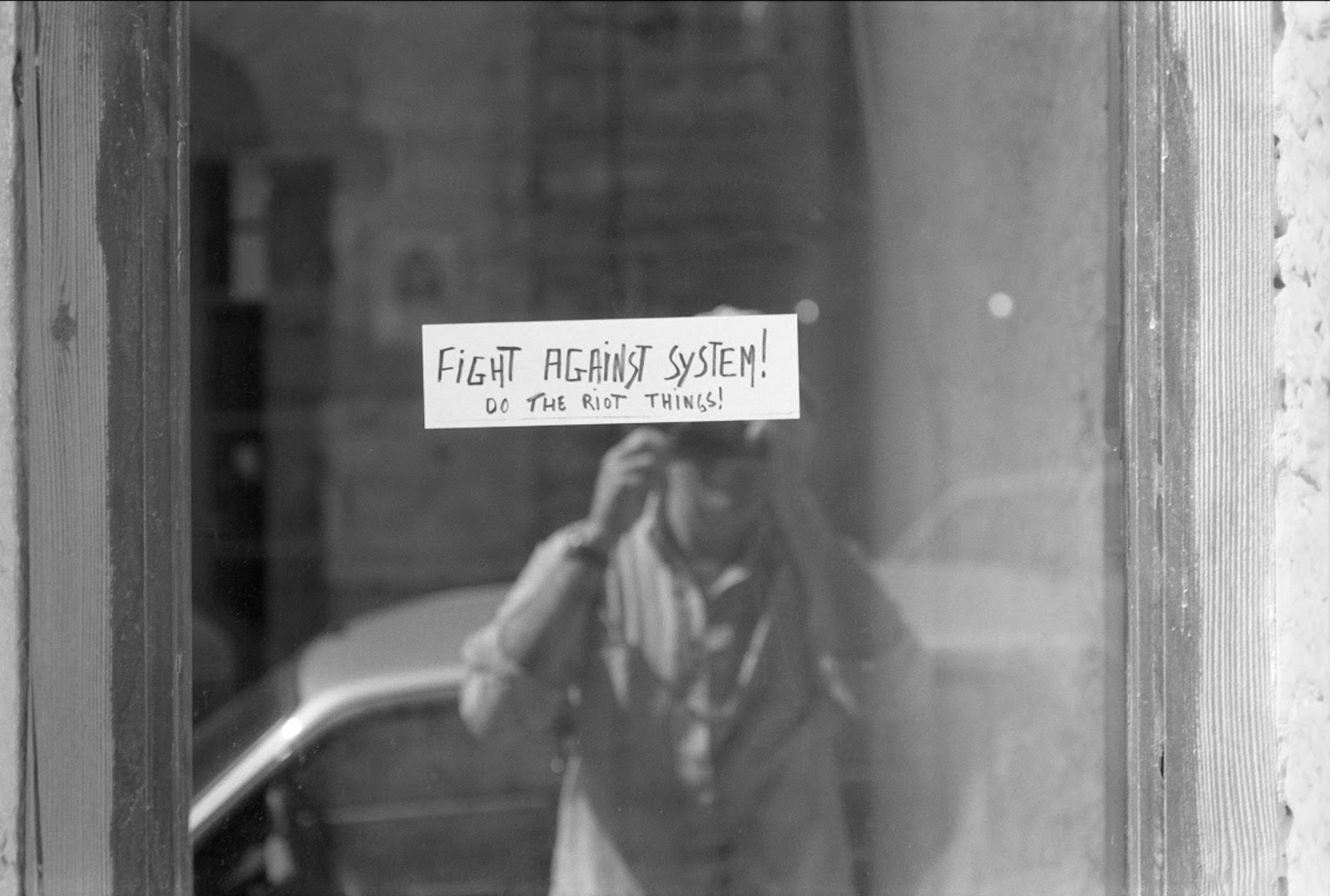 Black-and-white photograph of a pane of glass with a paper stuck to it that reads 