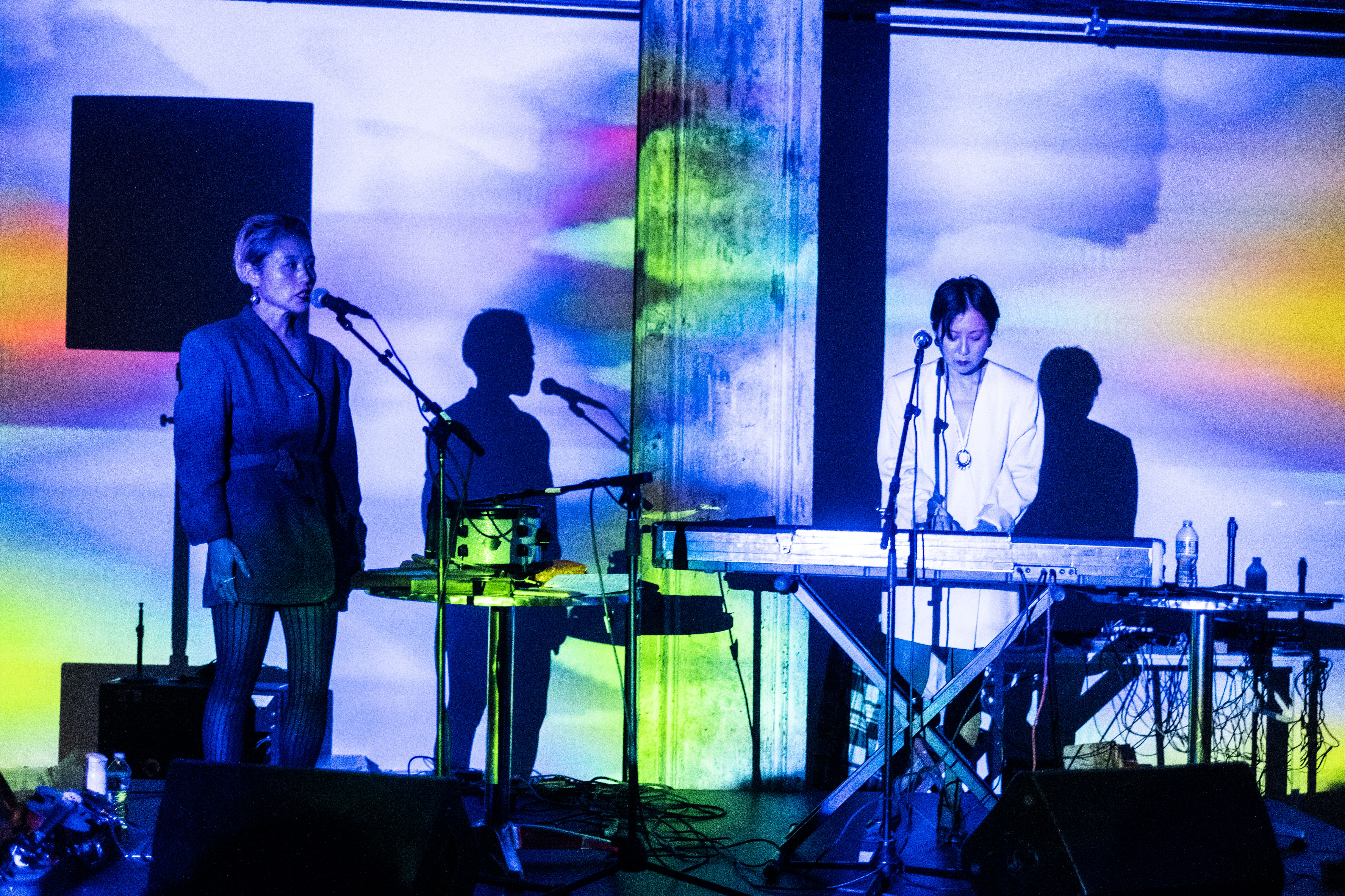 Two figures perform on a stage with a keyboard. Washes of blue, green, orange and pink light are projected onto them.