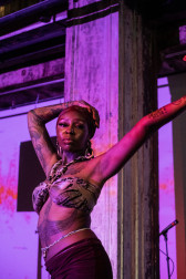 Portrait of a figure dancing on stage with purple projections cast onto them.