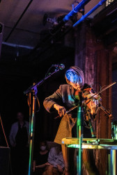 A figure plays the violin in front of a microphone.