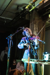 A figure plays the violin in front of a microphone.