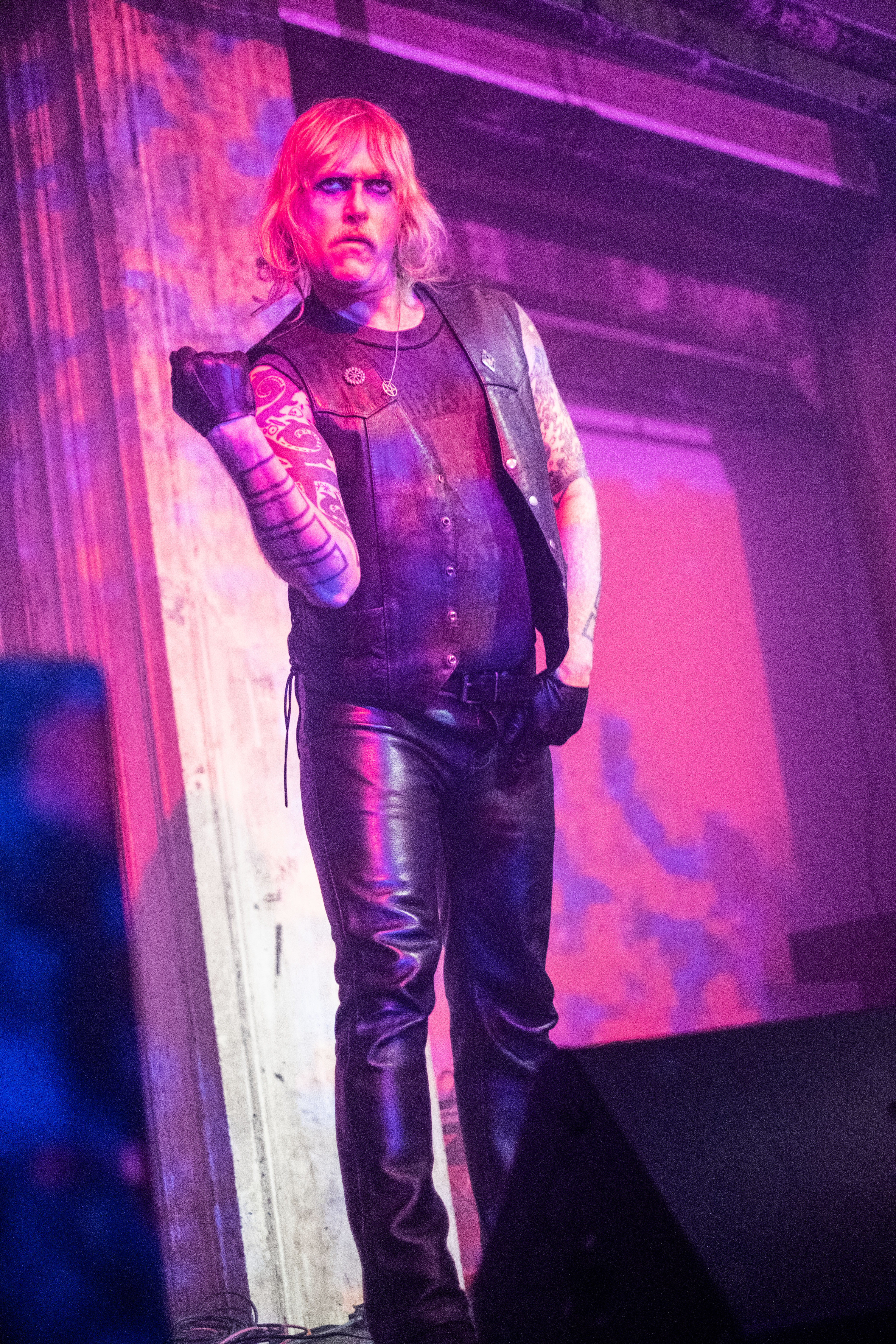 A figure dressed in leather performs on stage with a purple projection on them.