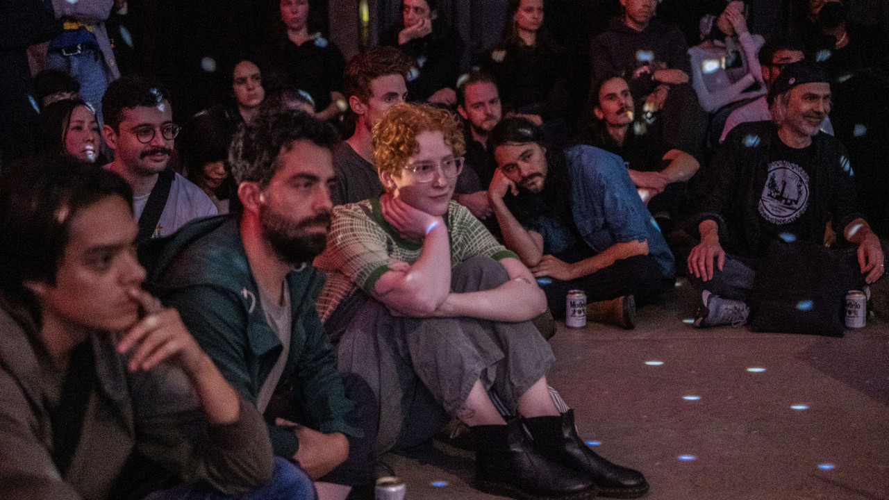 A color image of audience members sitting on the floor looking towards the stage. Blue light dots are projected onto them.