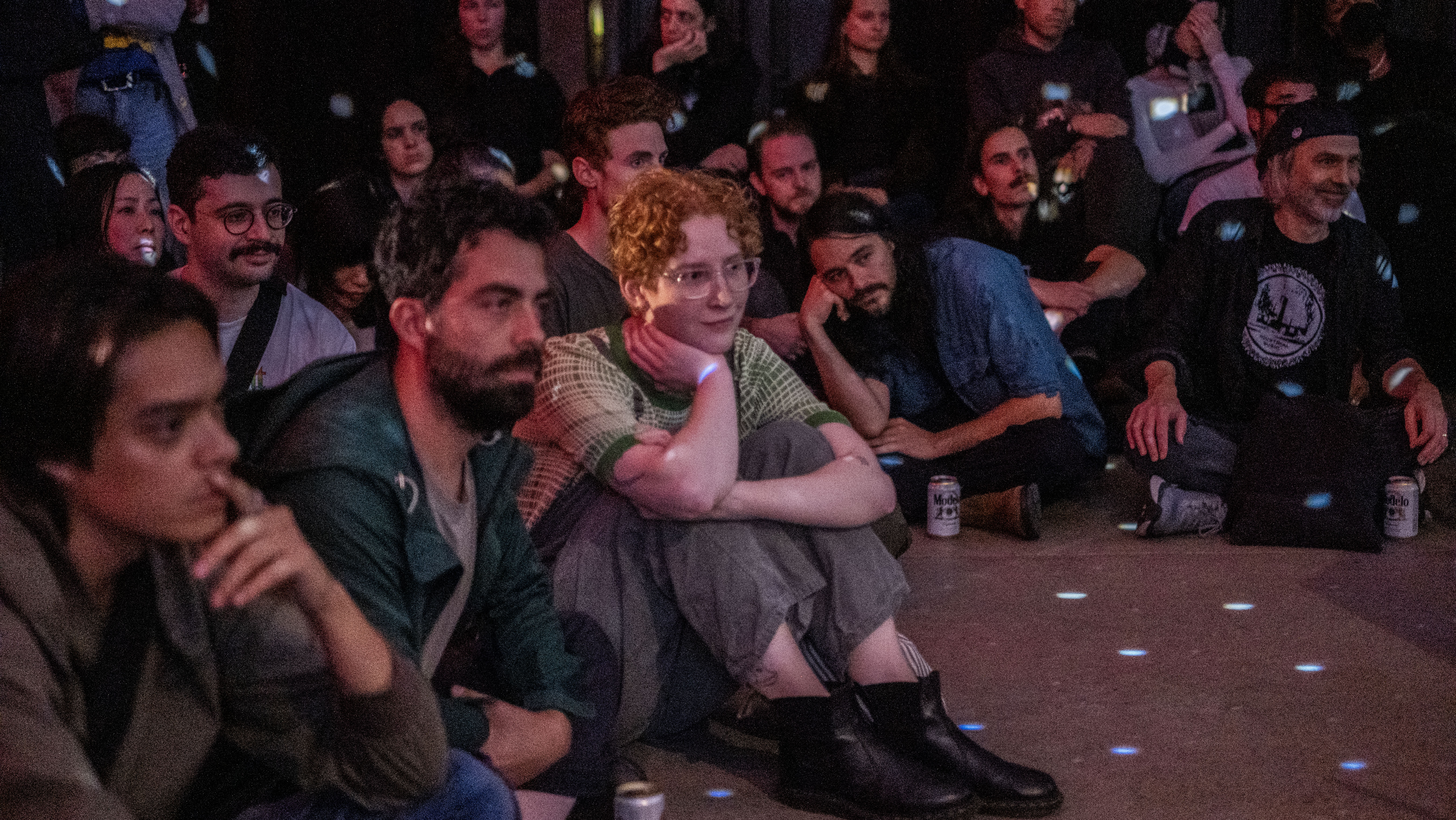 A color image of audience members sitting on the floor looking towards the stage. Blue light dots are projected onto them.