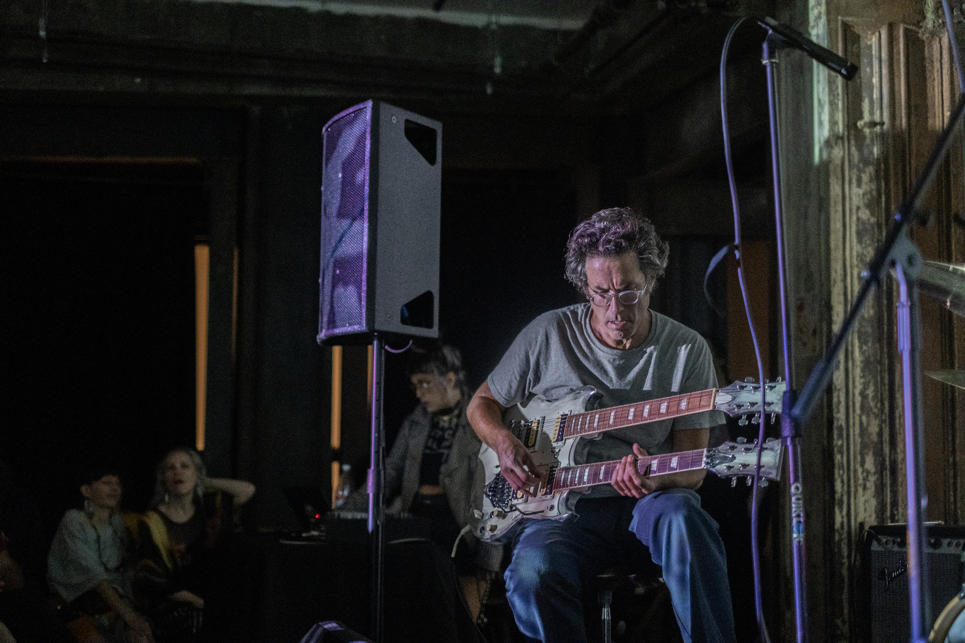 A performer sits on stage, playing a double-neck guitar.  