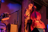 A performer plays the upright bass on stage. The stage and wall behind it are bathed in orange and blue light.
