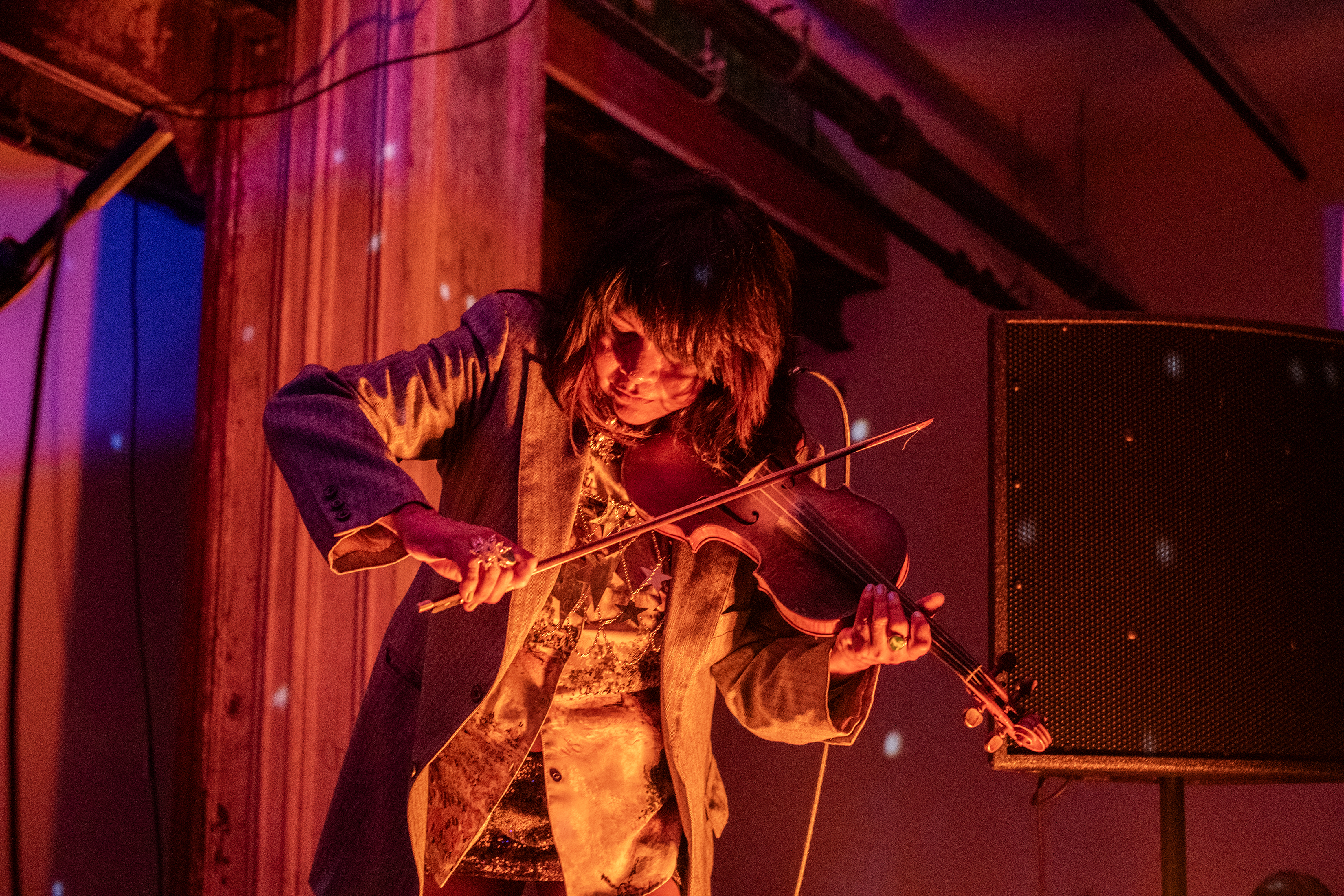 A performer plays the violin on stage. The stage and the wall behind it are bathed in orange light. 