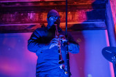 A performer plays a clarinet on stage, bathed in blue and pink light.