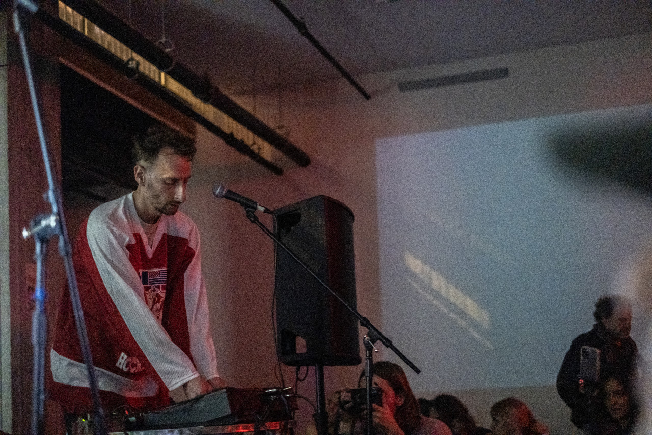 A performer on stage surrounded by equipment plays for an onlooking audience.