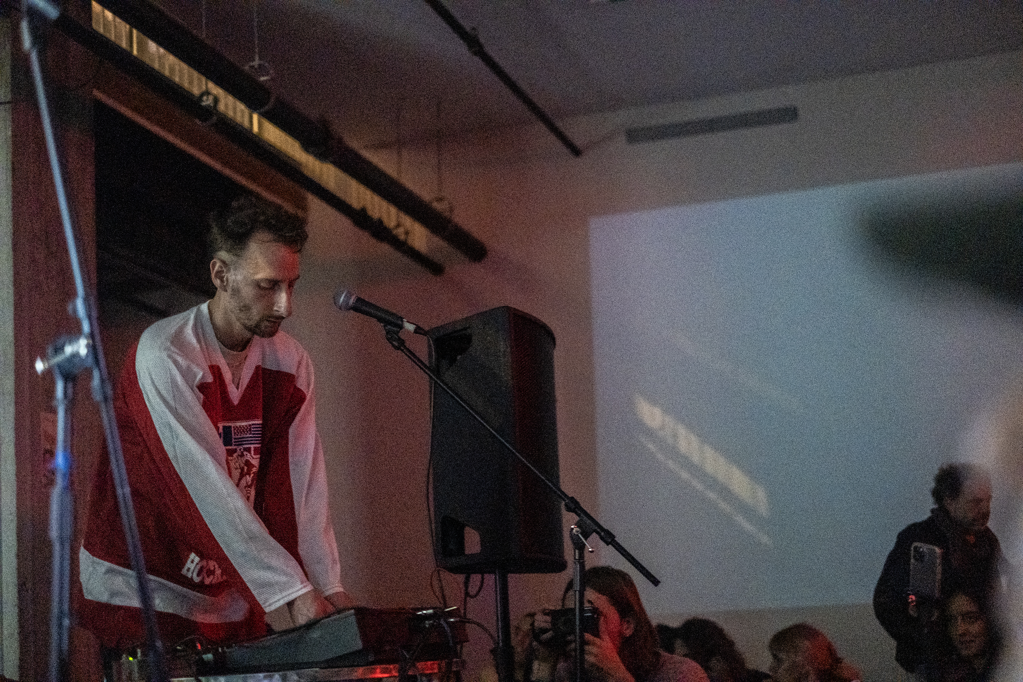 A performer on stage surrounded by equipment plays for an onlooking audience.