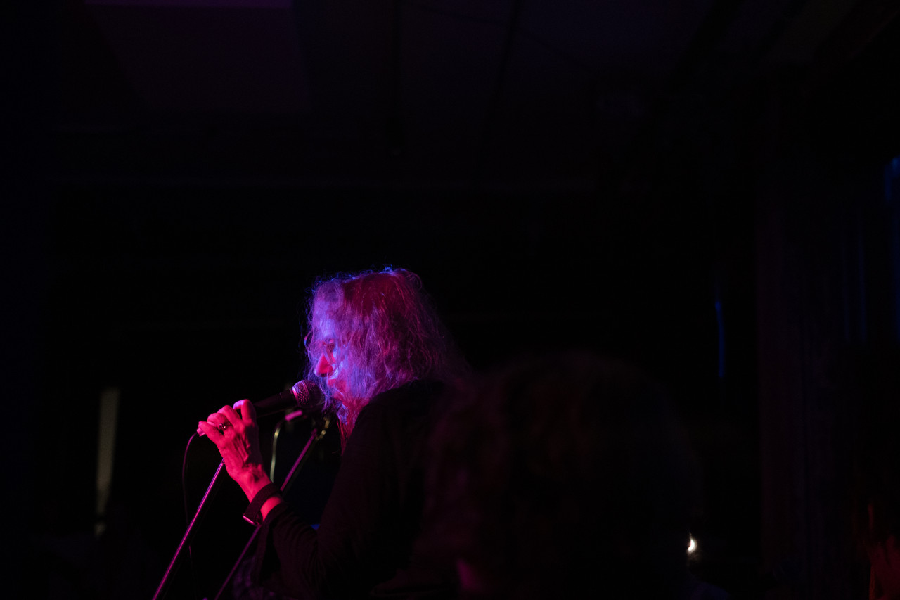A performer sings into a microphone solely illuminated by a red and blue light.