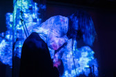 A performer sings onstage, obscured by hair and bathed in shades of blue light. 