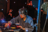 A performer manipulates a record while seated at a turntable.