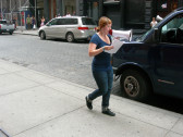 A person walking down a city street, speaking into a megaphone. Behind her are several cars and a small crowd of onlookers.