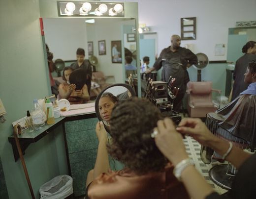 A woman looking at herself in a handheld mirror while getting a haircut at a barbershop