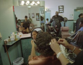 A woman looking at herself in a handheld mirror while getting a haircut at a barbershop