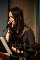 Portrait of a seated musician holding a microphone and a guitar.