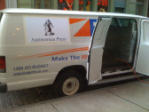 A Budget van is parked next to the curb with its side doors open. There is an orange extension cord coming out of the door, and a white paper taped on the side of the van with text, 