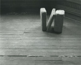 Installation view of three cast concrete blocks - the middle one leaning against the last one - standing on a wood floor.