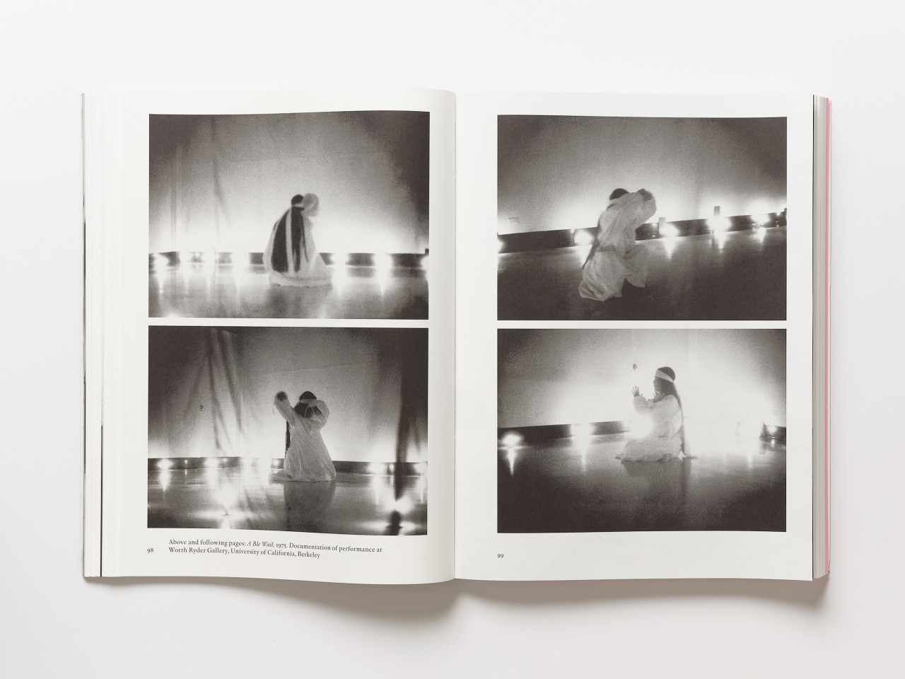A book lays open against a white background. The book pages feature four black-and-white photographs of a female figure dressed in white robes, performing various actions.