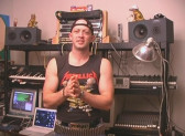 A man in a sleeveless Metallica shirt stands in front of a makeshift music studio, looking at the camera.