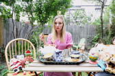 A woman in a pink dress sitting at a table in a yard surrounded by stuffed animals and a tea set.