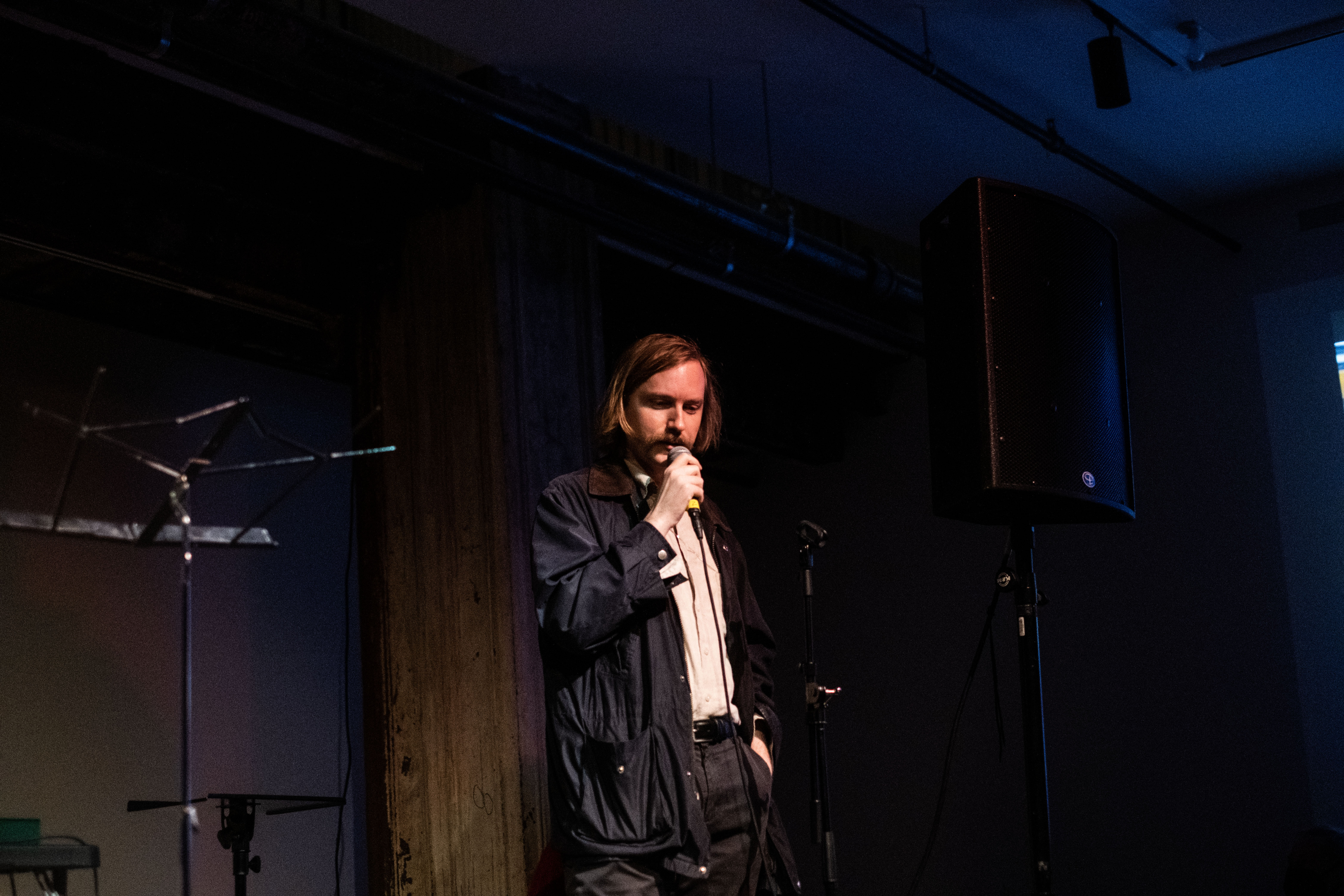 A figure stands on stage speaking into a microphone.