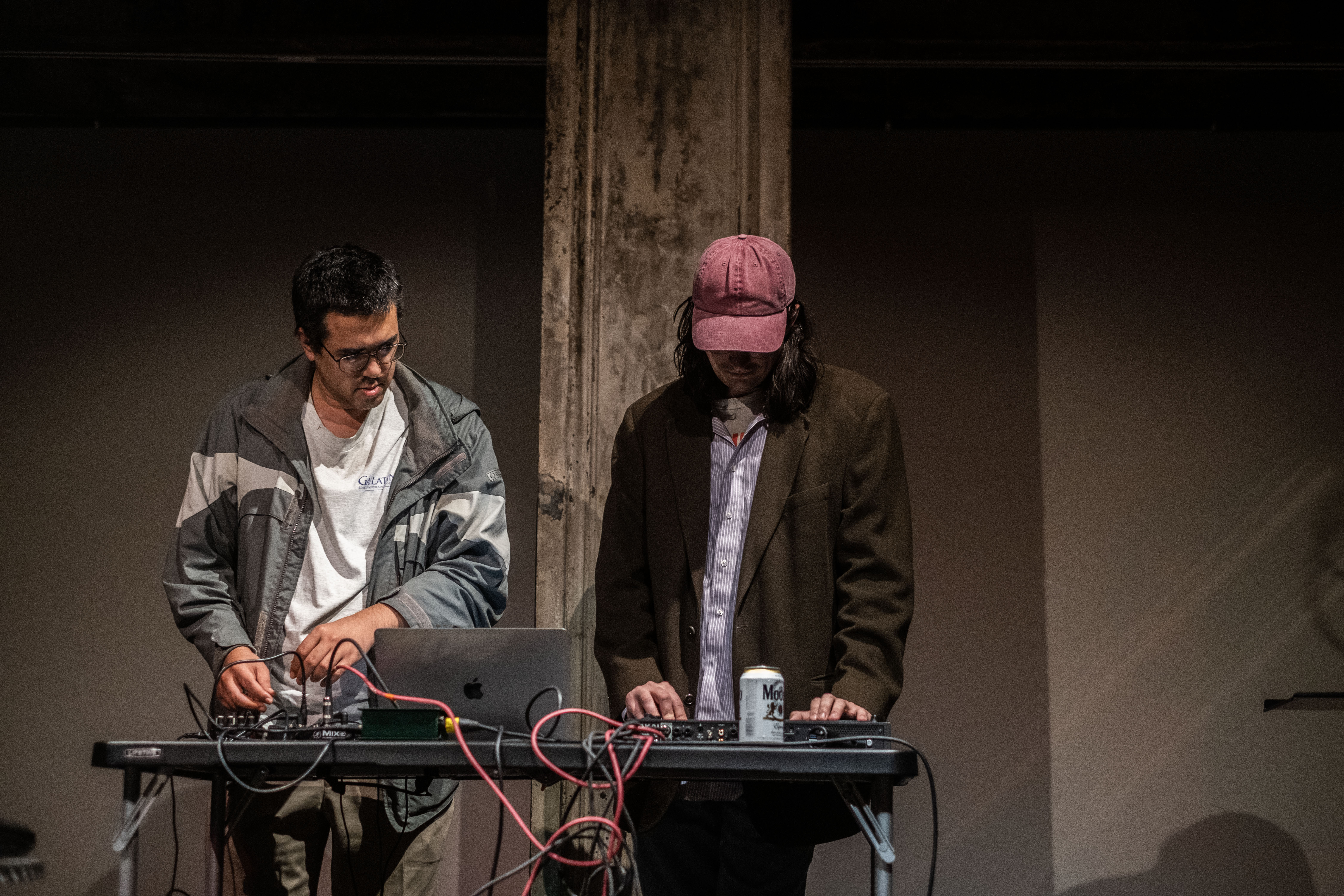 Two figures stand behind a table, setting up audio equipment.