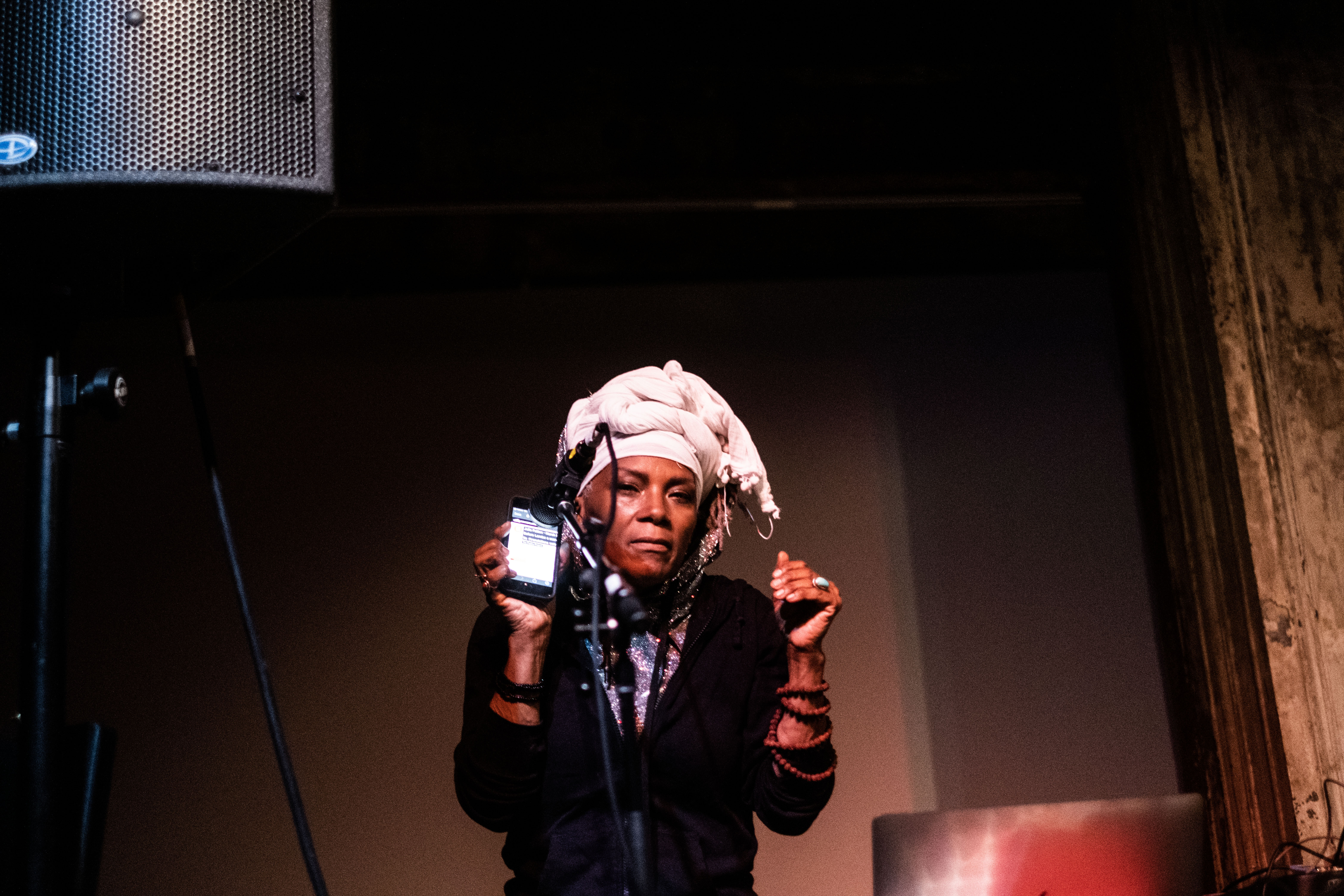 A figure performs on stage, holding their iPhone up to a microphone.