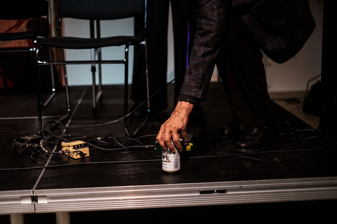 A figure leans down and places a beer can on the stage.