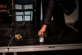 A figure leans down and places a beer can on the stage.