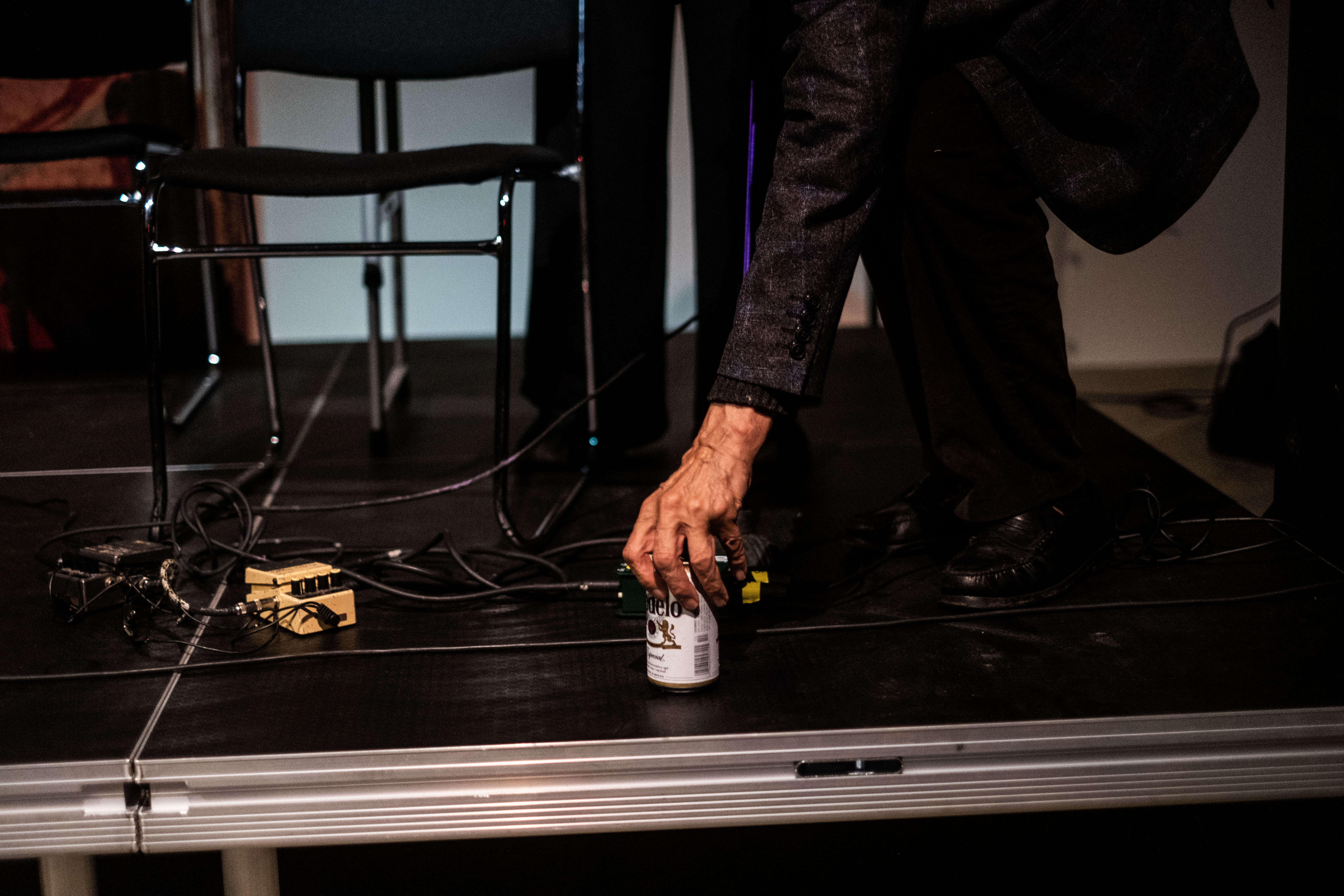 A figure leans down and places a beer can on the stage.