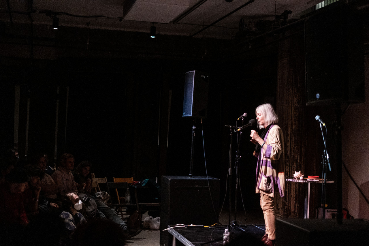 A figure to the right stands on stage and performs in front of an audience, shown to the left.