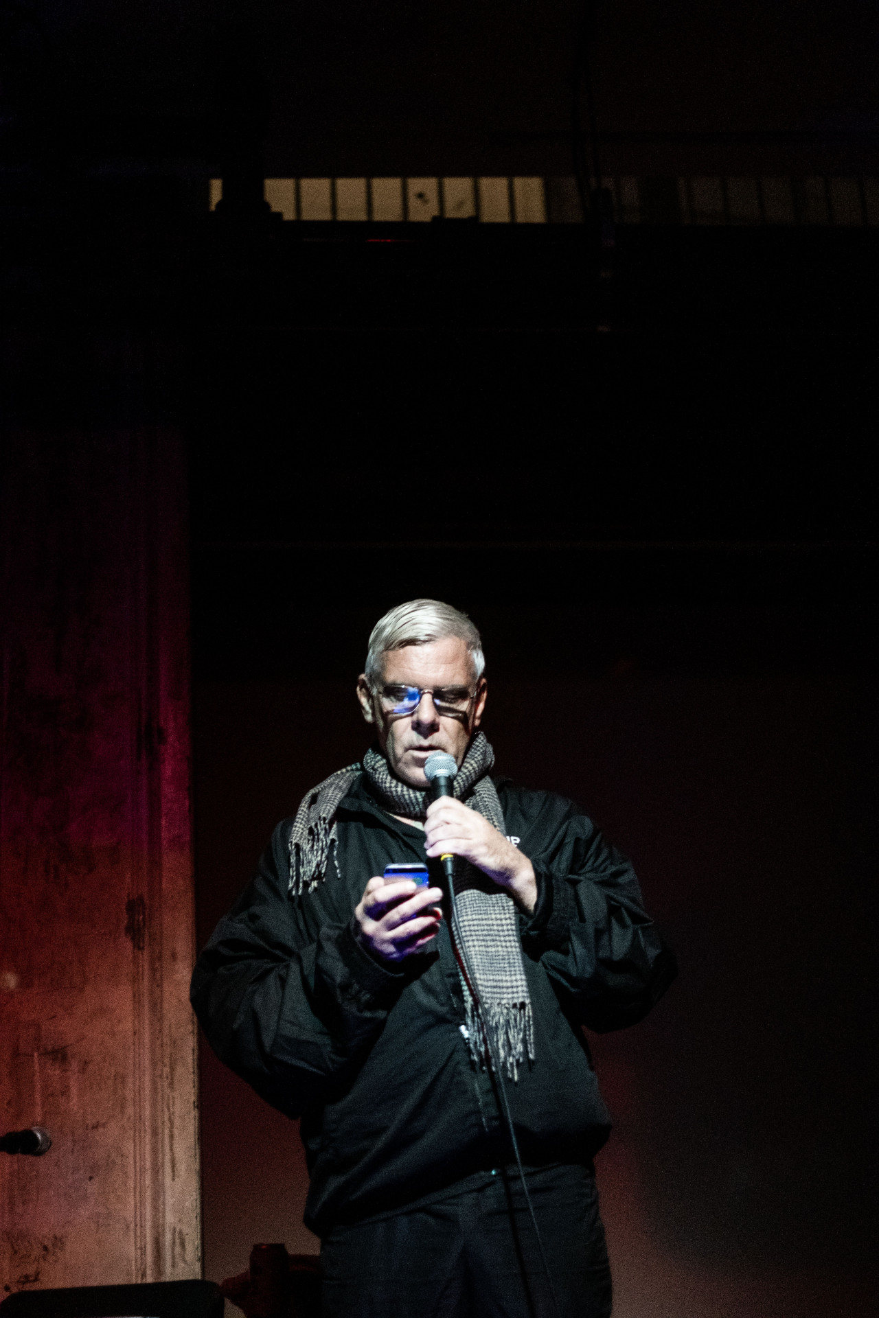 A figure reads into a microphone, glancing at their phone.