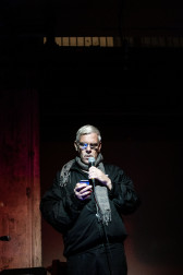 A figure reads into a microphone, glancing at their phone.