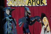 On the right, a figure speaking into a microphone appears to be in conversation with two humanoid blue birds.