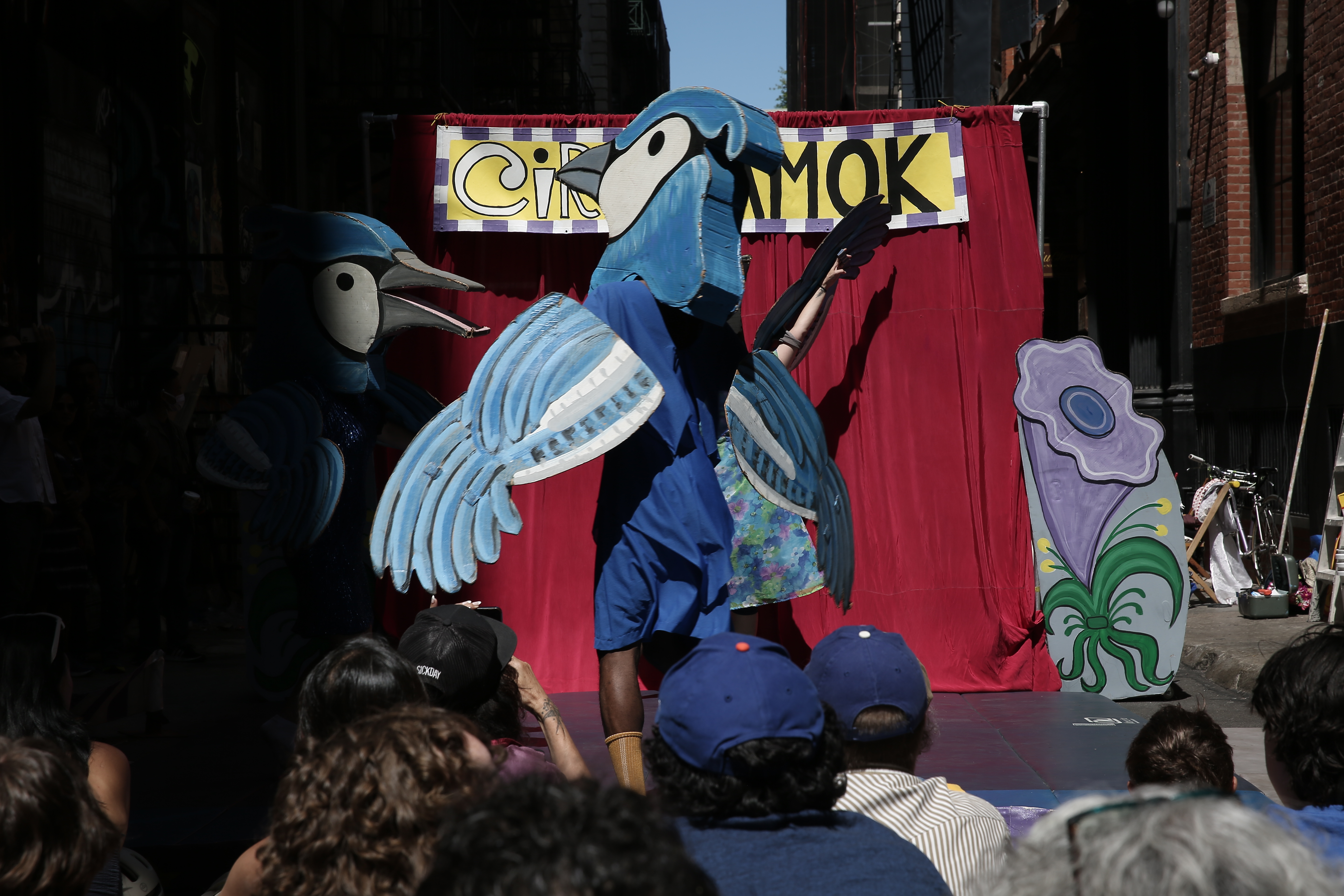 A crowd watches a large humanoid blue bird turn around.