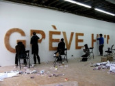 Five people, two standing and three in folding chairs, painting the partially formed words 